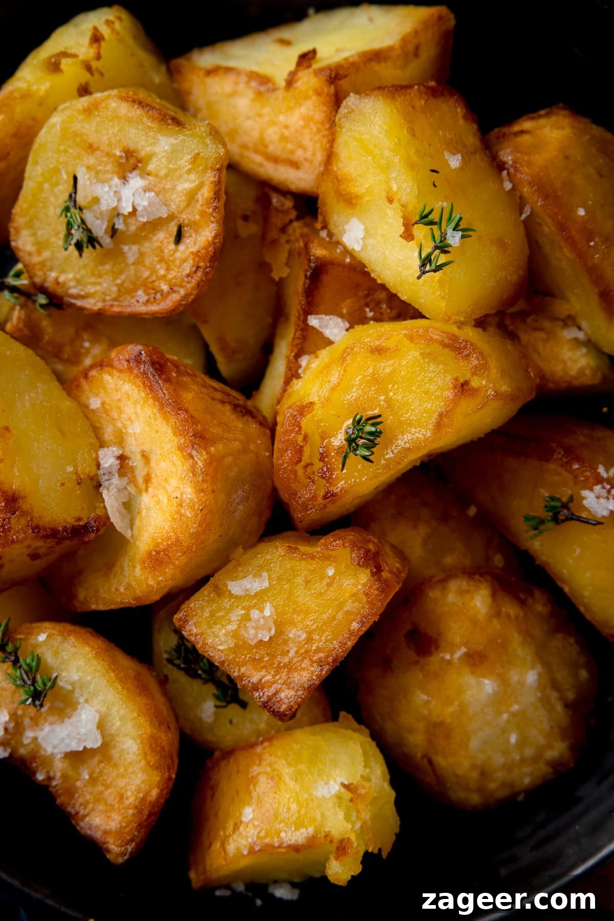 Ultra-Crisp Air Fryer Roast Potatoes 2 Close up overhead image of perfectly golden and crispy air fryer roast potatoes piled up in a dark bowl. The potatoes are generously sprinkled with fresh thyme and flaky sea salt, highlighting their irresistible texture.