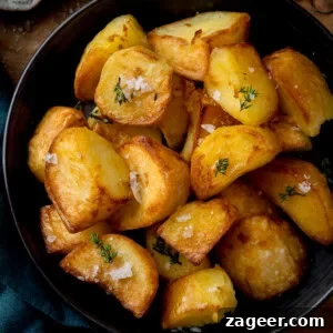 A bowl of golden air fryer roast potatoes, garnished with coarse salt and fresh herbs.