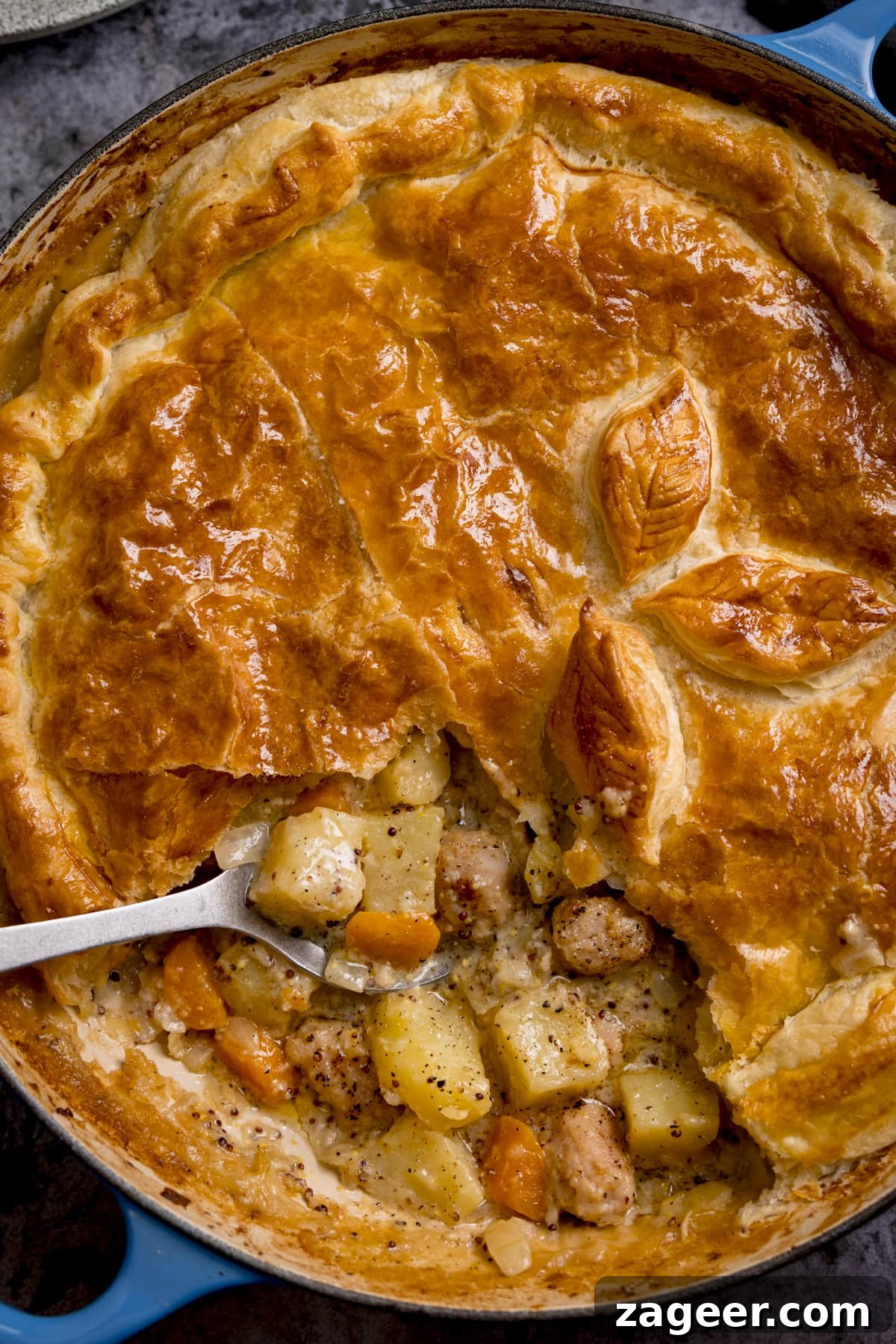 Artisan Sausage and Mustard Bake 5 Tall overhead image of a sausage and mustard pie with some of the pastry lid removed. There is a spoonful being taken from the pie.