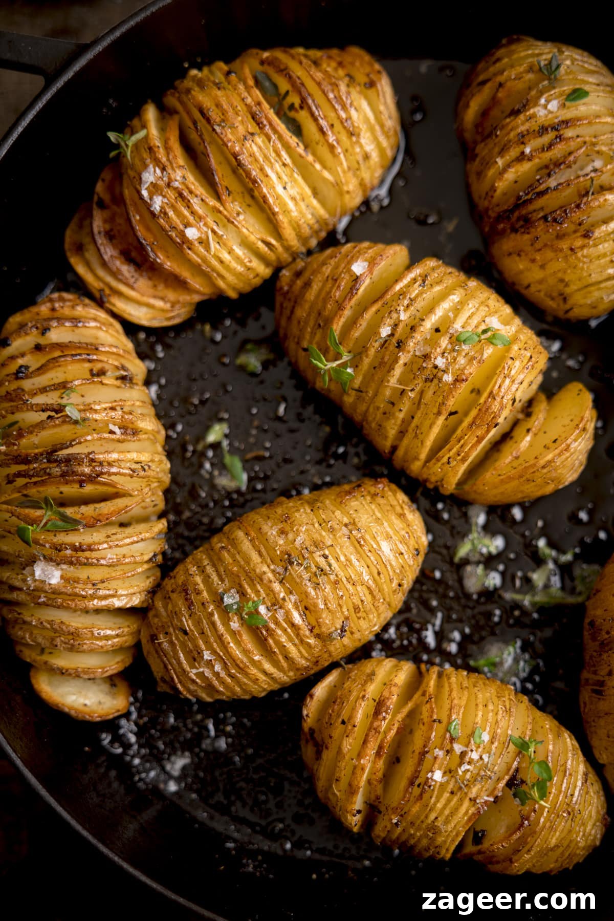 Crispy Accordion Potatoes 5 Overhead image of hasselback potatoes in a dark cast iron pan, topped with fresh thyme leaves and Maldon salt