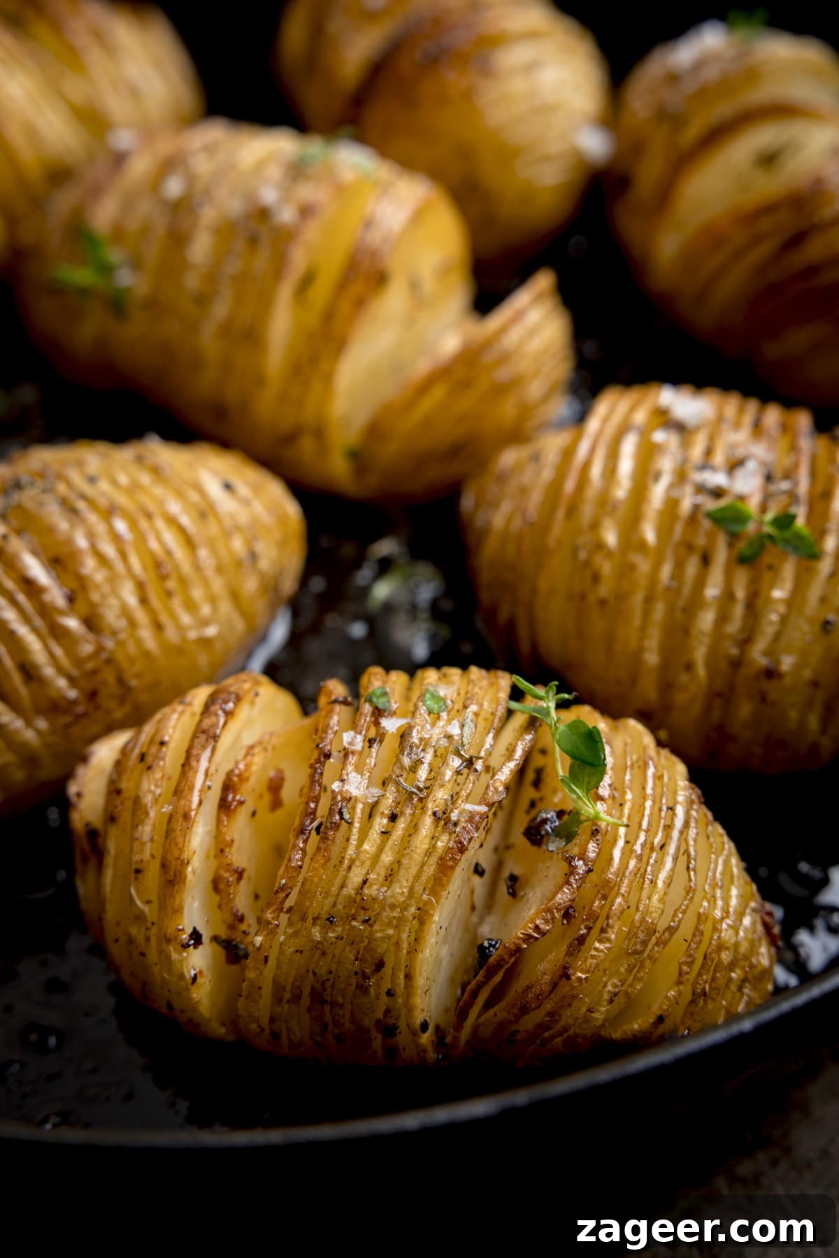 Crispy Accordion Potatoes 4 Close up image of hasselback potatoes in a dark cast iron pan, topped with fresh thyme leaves and Maldon salt