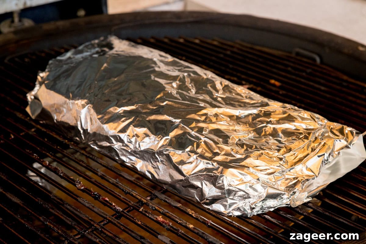 Smoky Dry Rub BBQ Ribs 8 A prep shot of BBQ Dry Rub Ribs. The ribs, now tightly wrapped in silver tin foil, are placed back on a black barbecue, which is maintained at 120 degrees Celsius. The foil package reflects the heat, ready for the tenderizing phase of cooking.
