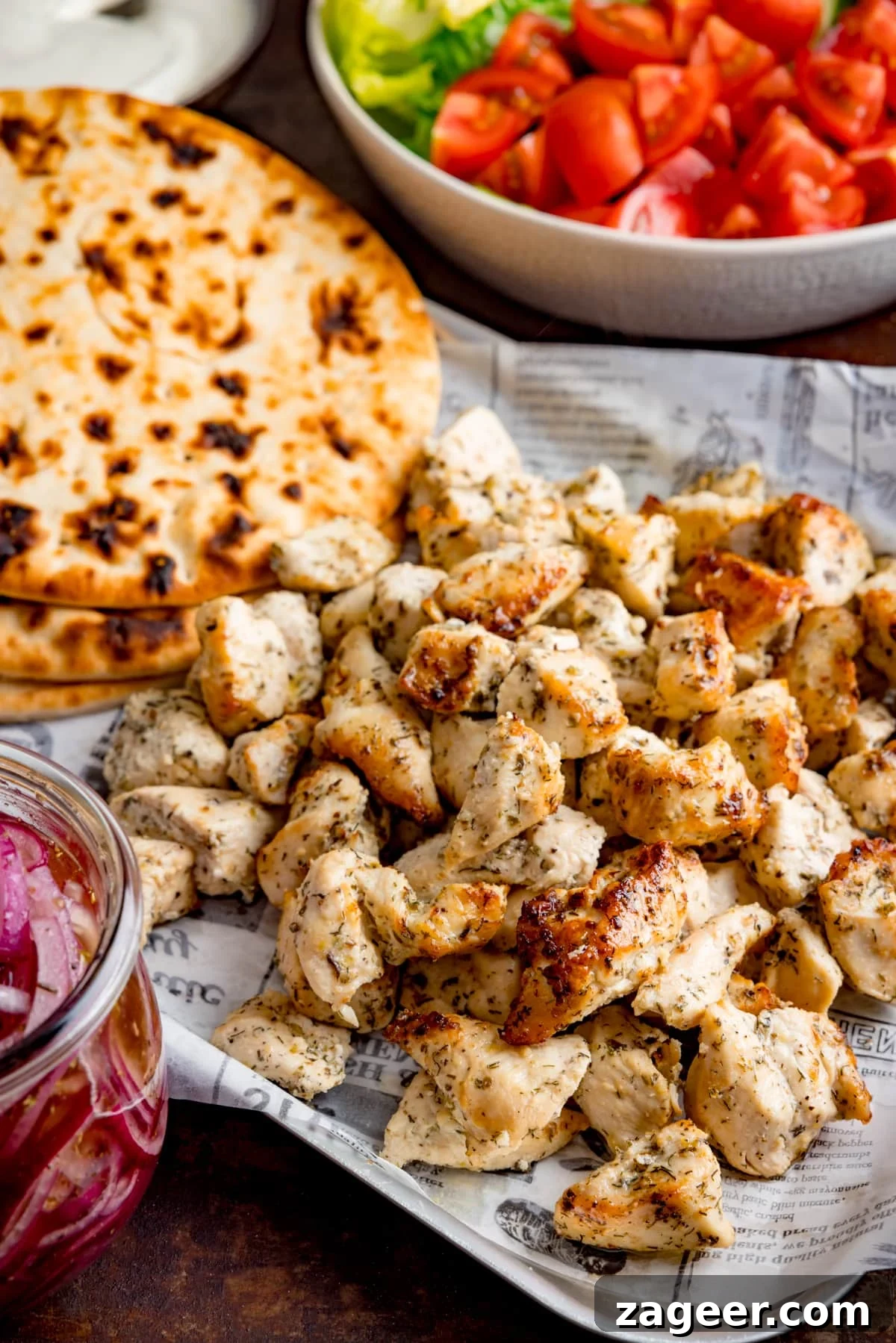 Lemon Herb Air Fryer Greek Chicken 2 Air fryer Greek chicken pieces on a tray with flatbreads, a bowl of tomatoes and lettuce, and a jar of marinated onions, showcasing a complete meal ready to be enjoyed.