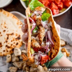 Square overhead shot of air fryer Greek chicken pieces in a flatbread with salad and feta dressing. The wrap is being held by a hand over the top of a tray that has all of the cooked ingredient on it.
