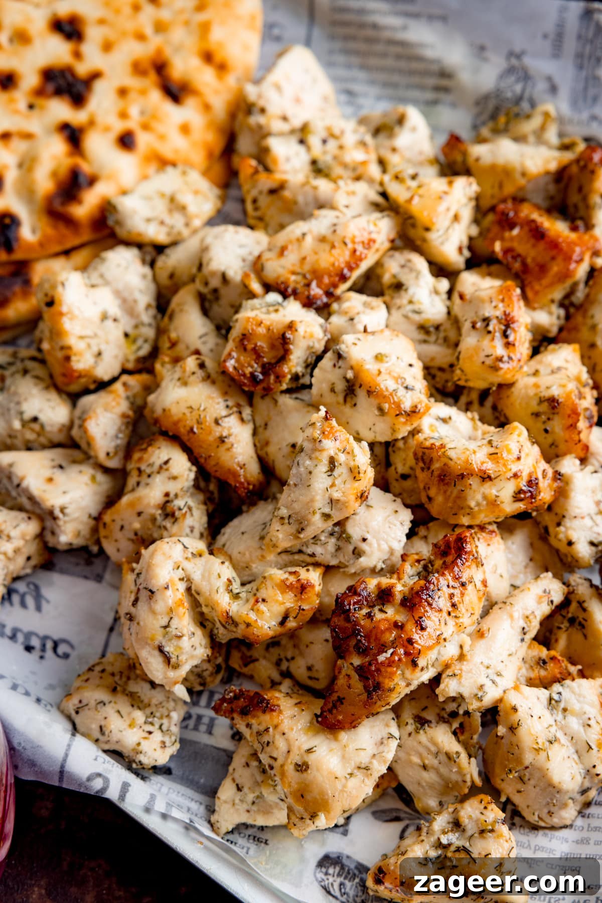 Lemon Herb Air Fryer Greek Chicken 4 Close-up image of beautifully air-fried Greek marinated chicken pieces arranged on a tray lined with parchment paper, accompanied by warm flatbreads, ready for assembly.