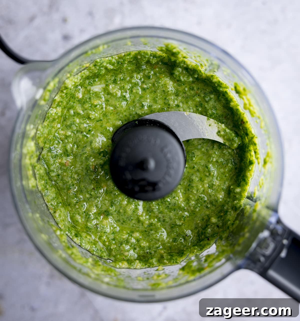 Effortless Pesto Pasta Perfection 4 Overhead shot of homemade pesto in a small food processor, on a light background.