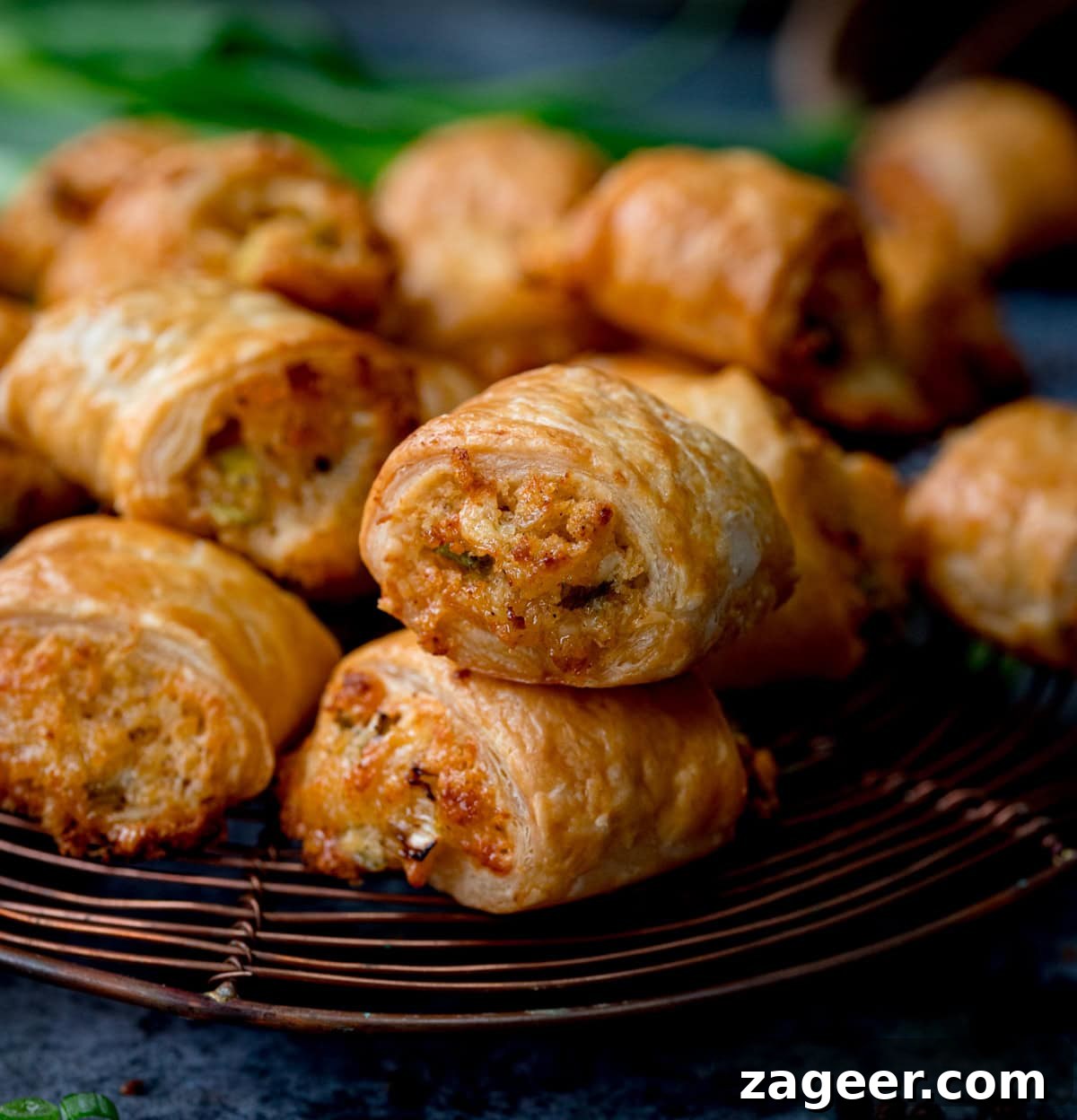 The Secret to Vegetarian Sausage Rolls That Meat Eaters Crave 2 A close-up of several golden-brown, crispy vegetarian sausage rolls, freshly baked and stacked on a wire cooling rack, with a soft, blurred background.