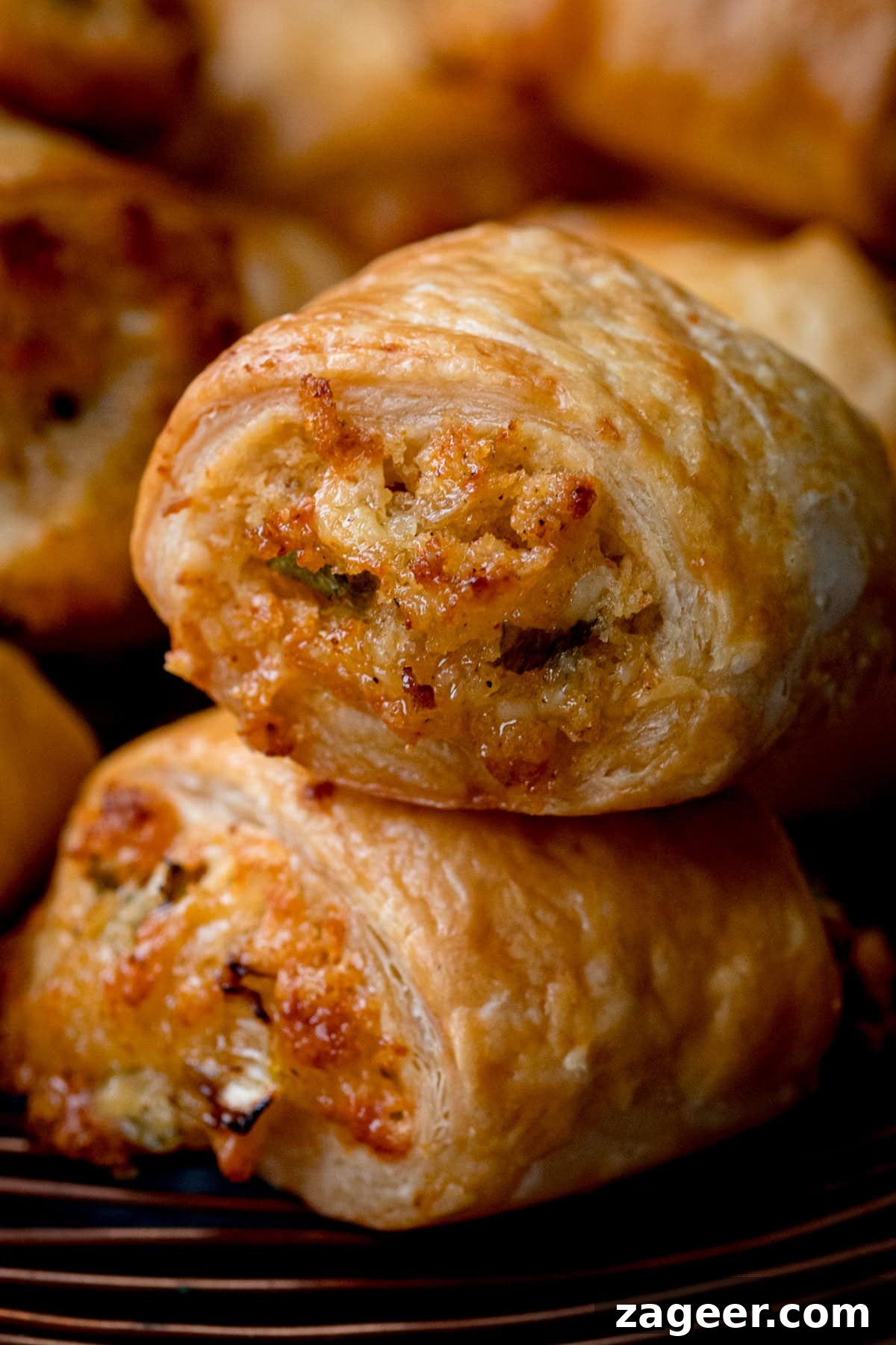 The Secret to Vegetarian Sausage Rolls That Meat Eaters Crave 13 Close-up of two golden-brown puff pastry vegetarian sausage rolls stacked on top of each other, showcasing their flaky layers and visible savory cheese and onion filling.