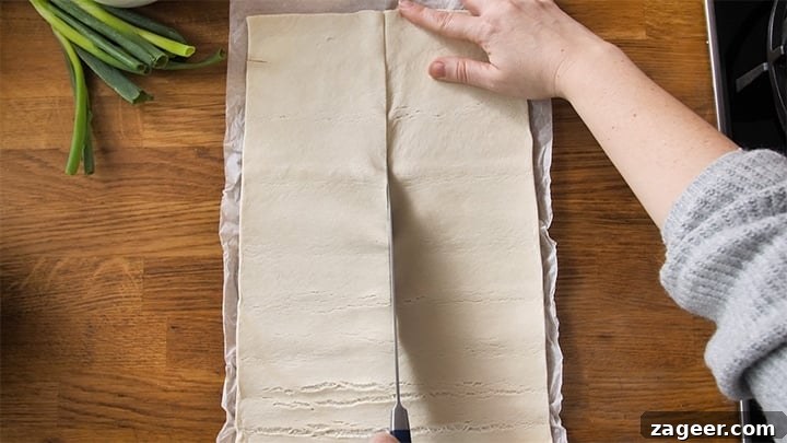 The Secret to Vegetarian Sausage Rolls That Meat Eaters Crave 6 A sheet of ready-rolled puff pastry being expertly cut in half lengthwise on its parchment paper.
