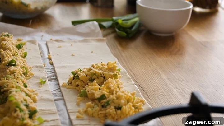 The Secret to Vegetarian Sausage Rolls That Meat Eaters Crave 7 A generous line of cheesy filling being spooned onto a strip of puff pastry, ready to be rolled into vegetarian sausage rolls.