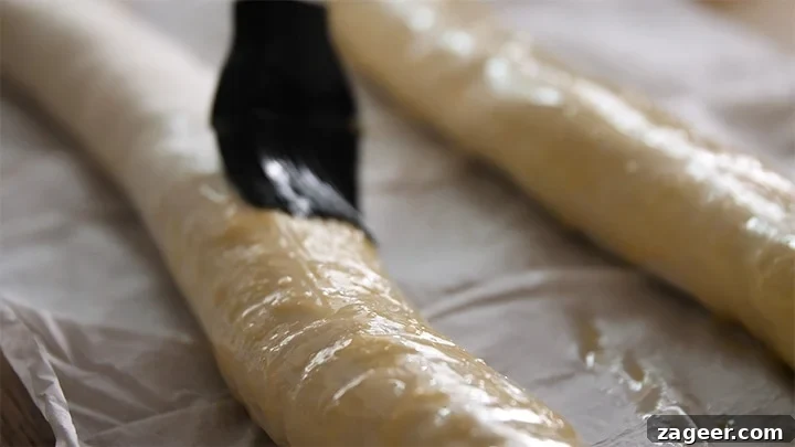 The Secret to Vegetarian Sausage Rolls That Meat Eaters Crave 10 A pastry brush applying a glistening egg wash over a long vegetarian sausage roll, preparing it for baking.