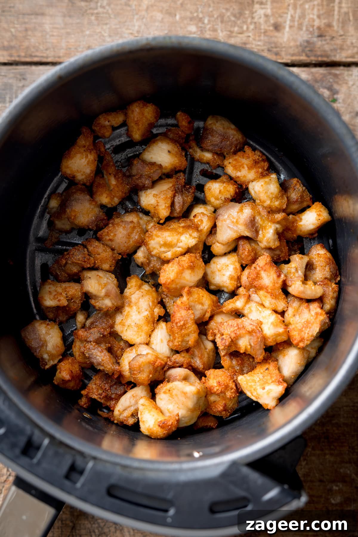 Crispy Air-Fried Sesame Chicken 4 Overhead image of crispy air fryer chicken pieces in an air fryer basket. The basket is on a wooden background.