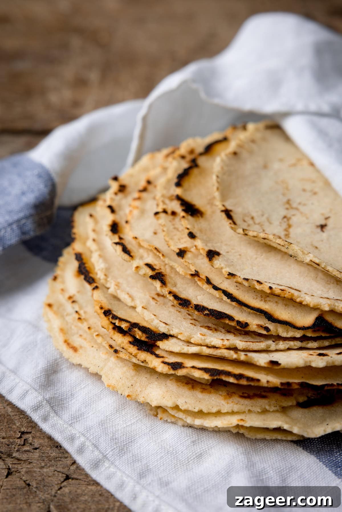 Perfect Homemade Corn Tortillas 2 A beautiful stack of nine golden-yellow homemade corn tortillas, gently resting on a white and blue striped napkin, all arranged on a rustic wooden surface, highlighting their fresh, warm, and inviting texture.