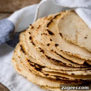 Perfect Homemade Corn Tortillas 10 A stack of golden corn tortillas on a blue and white striped napkin, ready to be served, symbolizing fresh, homemade goodness.