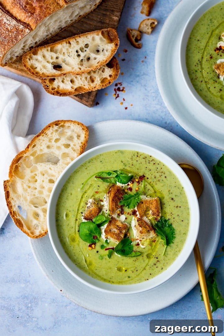 Velvety Broccoli Cream 2 Broccoli soup in a bowl topped with croutons and baby salad leaves on a light blue background, served with freshly sliced bread
