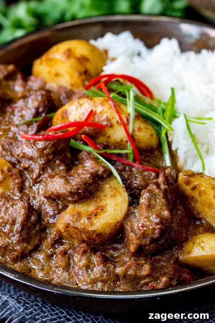 Slow-Simmered Beef Massaman Curry 3 Close-up view of a bowl of Slow Cooked Beef Massaman Curry, showing the tender beef and potatoes, served with rice and a sprinkle of chilli for garnish.