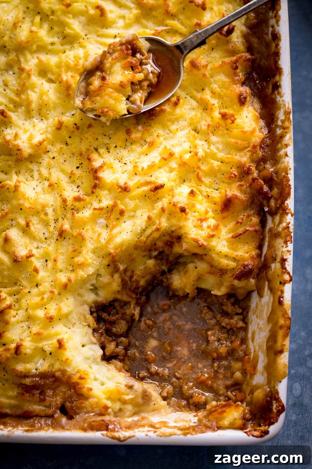 Cozy Homemade Shepherd's Pie 2 Close-up of a golden-brown Shepherd's pie with a portion removed, revealing the rich lamb filling. A spoon rests on top with a scoop of pie.