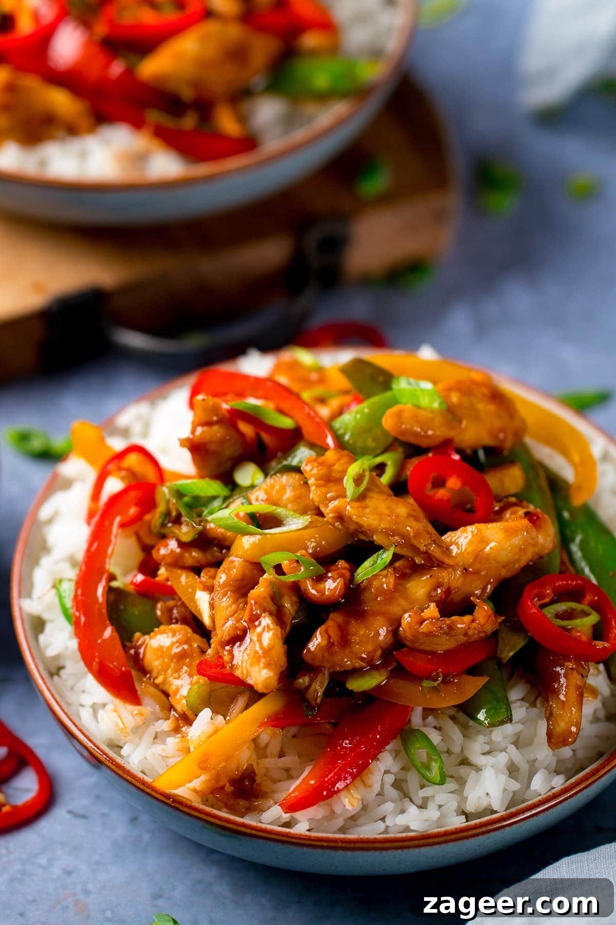 Fast & Flavorful Chicken Stir-Fry 5 A beautifully plated chicken stir fry in a bowl, topped with chopped chillies and spring onions, alongside a separate bowl of steamed white rice, ready for serving.