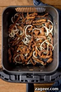 Crispy Air-Fried Chili Beef 5 Strips of crispy beef and cooked onion slices in an air fryer basket, viewed from above.