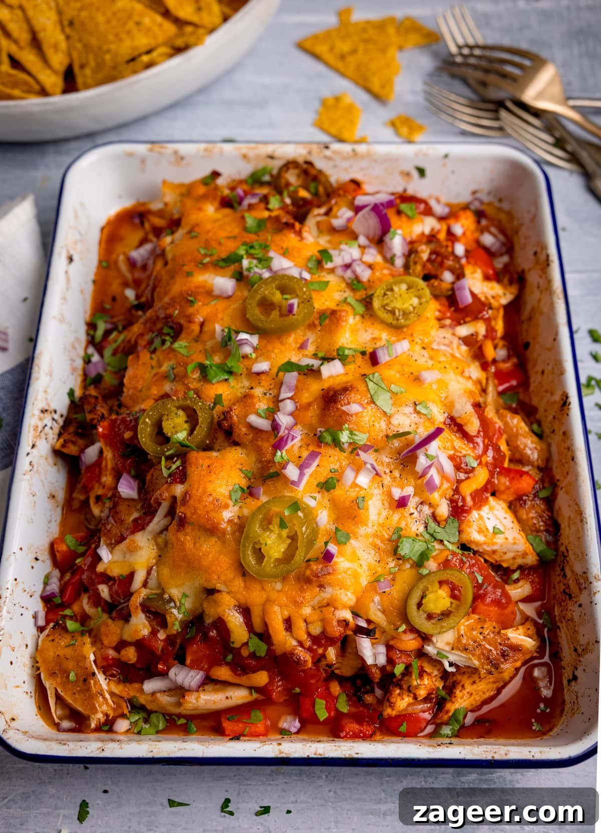Fiesta Chicken 5 A vibrant baking dish filled with a cheesy salsa chicken bake, beautifully topped with melted cheese, bright green jalapeños, finely diced red onions, and fresh chopped coriander. Red peppers and a rich tomato sauce are also visible, creating an inviting, colorful meal.
