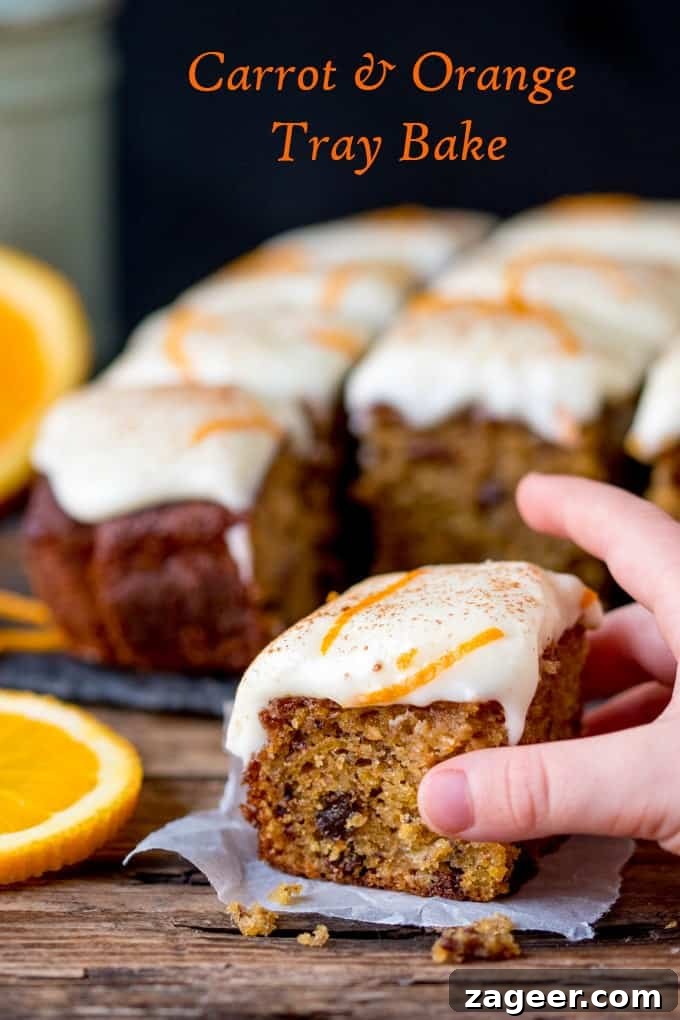 Orange Zest Carrot Traybake with Citrus-Soaked Raisins 2 A hand reaching for a piece of fluffy carrot tray bake, showcasing orange-infused raisins and thick zesty cream cheese frosting