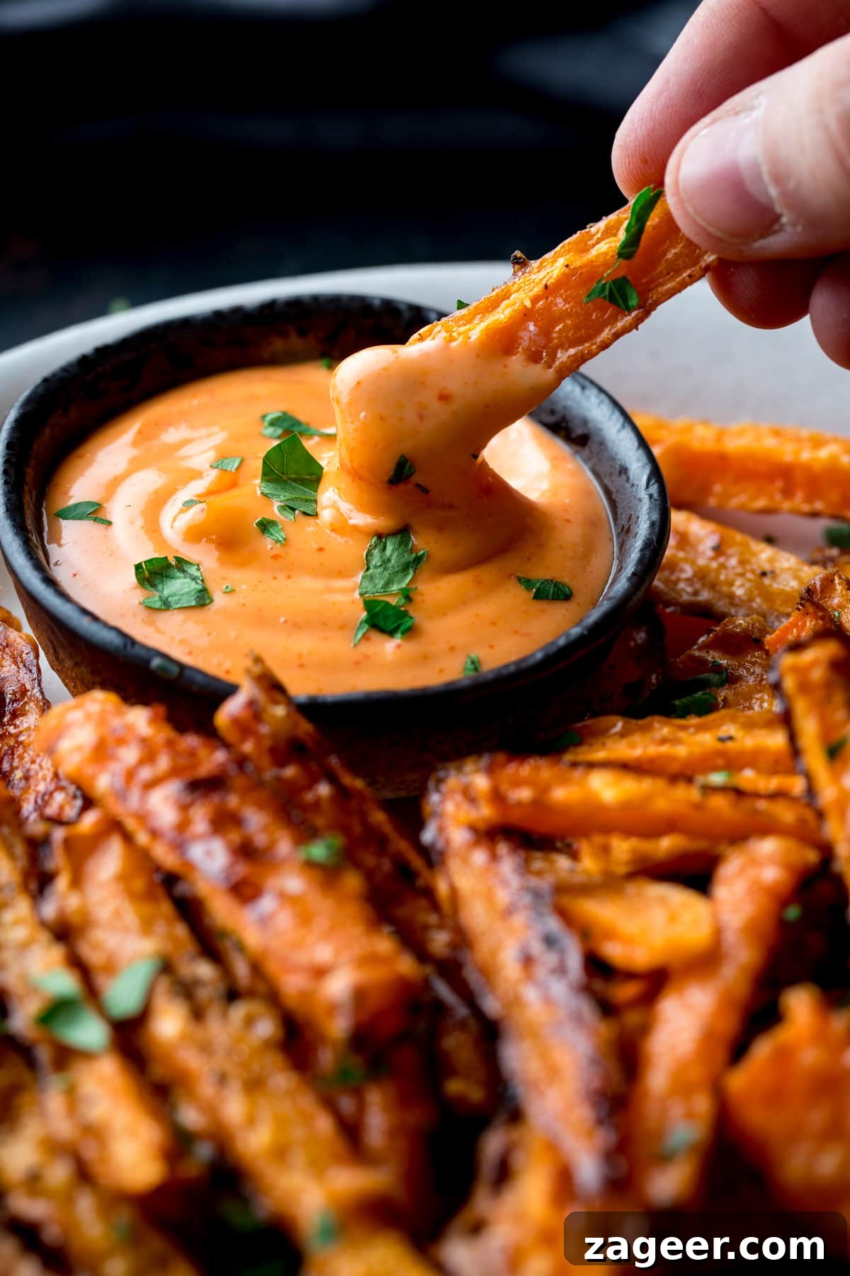 Golden Parmesan Carrot Fries 6 A close-up of a single baked parmesan carrot fry being dipped into a small bowl of creamy red sriracha mayo.