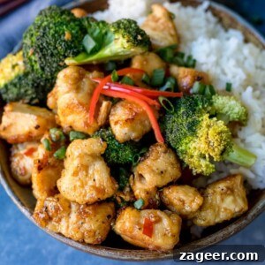 Square image of Asian crispy chicken with broccoli and rice in a stoneware bowl. Blue napkin in background