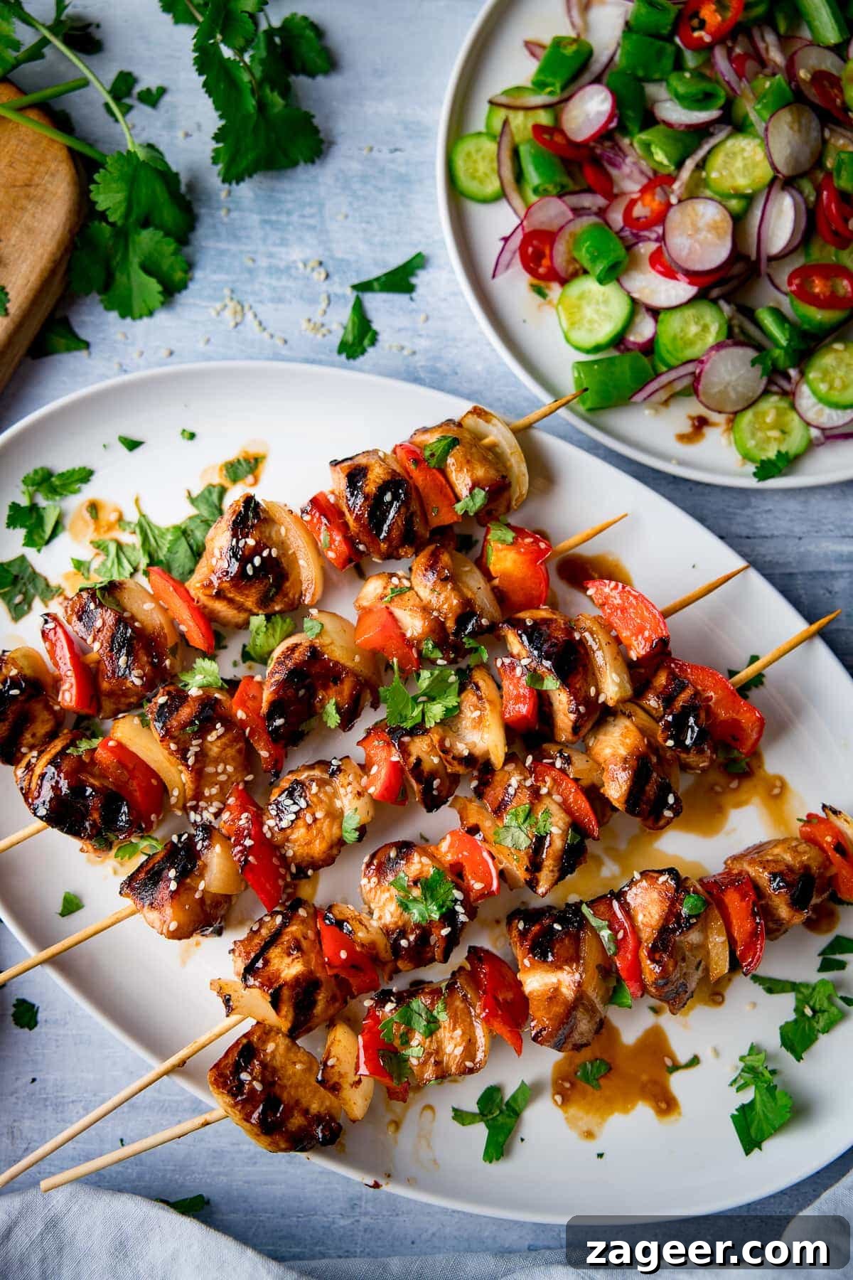 Sticky Honey Garlic Chicken Skewers 2 Close-up of golden brown honey garlic chicken skewers garnished with sesame seeds and fresh coriander on a white plate