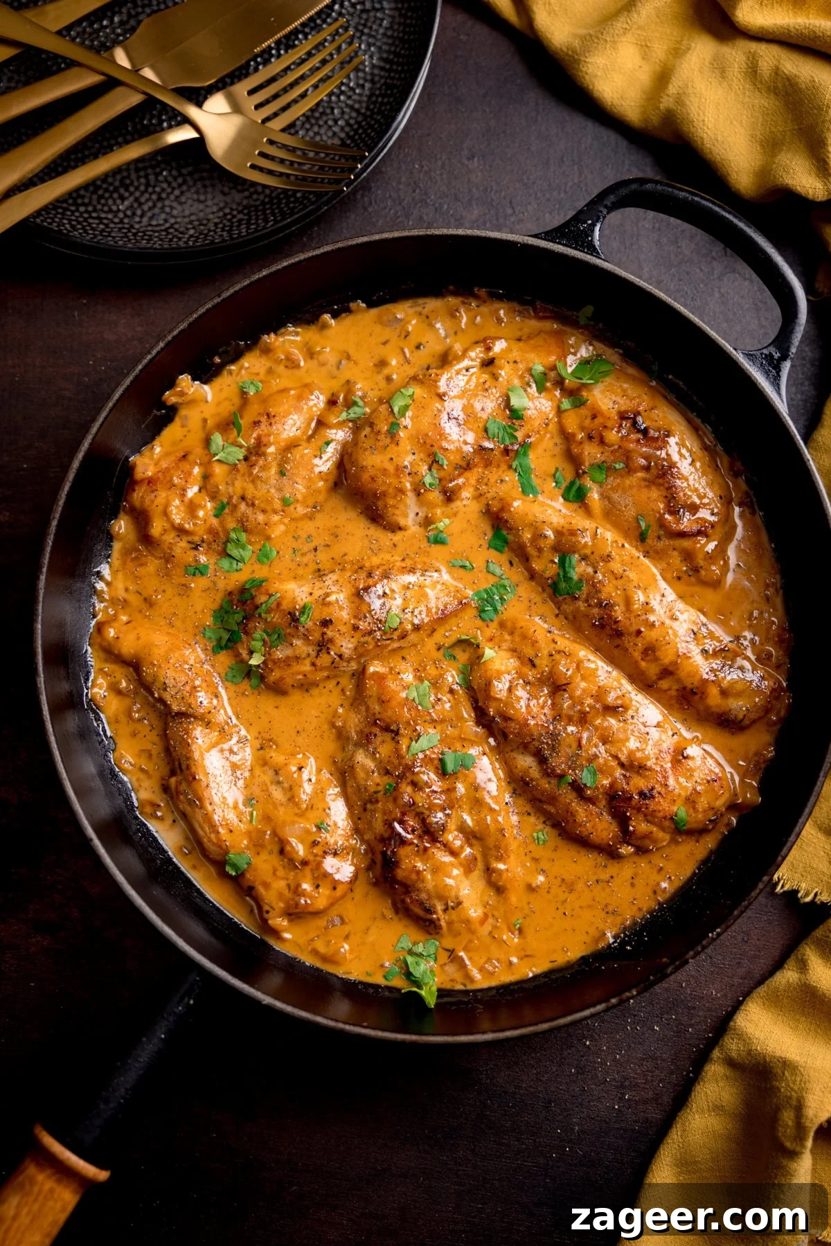 Golden Glazed Honey Mustard Chicken 5 Creamy honey mustard chicken garnished with chopped herbs, served in a black frying pan on a dark table with gold cutlery and a yellow serviette nearby.