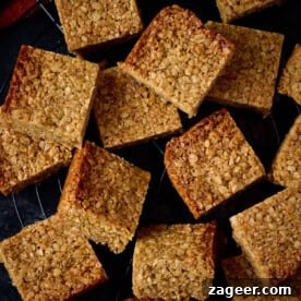 A close-up view of several golden, chewy flapjacks with a rustic, oat-rich texture, appealingly arranged to invite a comforting snack break. The light reflects on their glossy, syrupy surface.