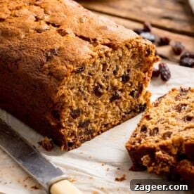 A close-up shot of a generously sliced moist and fruity tea loaf on a warm wooden table, highlighting its rich texture and abundant fruit. The image invites a delicious tea-time treat, promising a comforting experience.