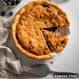 An inviting overhead shot of a vibrant blueberry crumble pie, with a single slice perfectly removed, revealing the rich, juicy fruit filling and the golden, textured crumble topping. The remaining pie shows its rustic charm and generous filling.