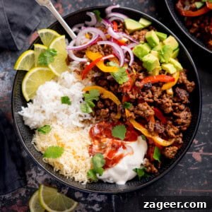 A vibrant and fully loaded minced beef fajita bowl, featuring fluffy white rice, savory spiced minced beef with peppers, a generous topping of grated cheese, and fresh garnishes including sliced red onion, avocado cubes, and lime wedges. A dollop of sour cream and a spoonful of salsa add creamy and zesty notes, all brightened with a sprinkle of fresh coriander.