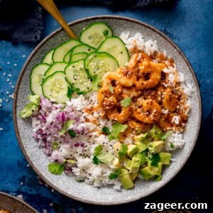 A bowl of white rice topped with cooked honey garlic prawns, sliced cucumber, chopped red onion, diced avocado, fresh coriander, and sesame seeds.