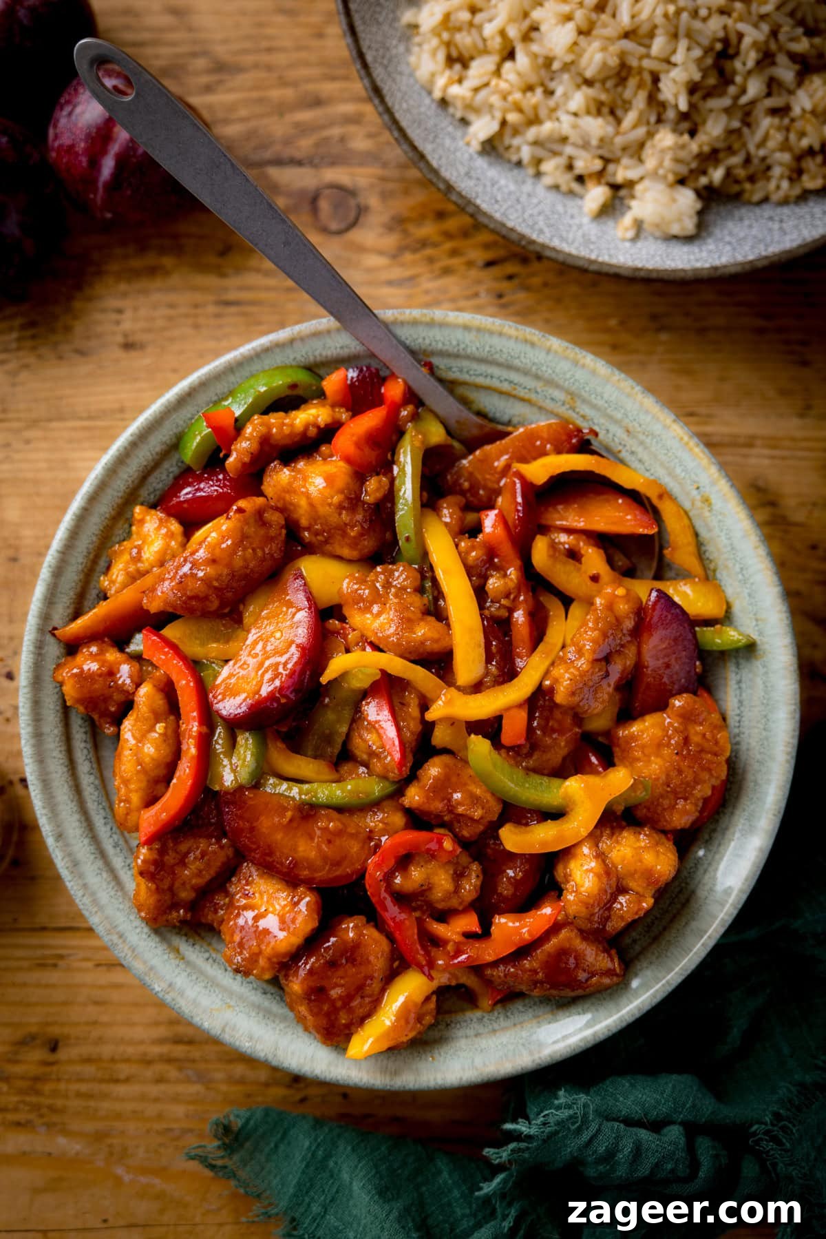 Imperial Plum Chicken Stir-Fry 5 A bowl of Chinese chicken plum stir-fry with red, yellow, and green peppers in a bowl on a wooden table. A green napkin is at the bottom of the shot.