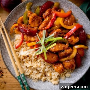 Imperial Plum Chicken Stir-Fry 7 Chinese plum chicken stir fry and rice in a shallow bowl with strips of spring onion on top. There is a set of chopsticks on the side of the bowl. The bowl is on a wooden table.