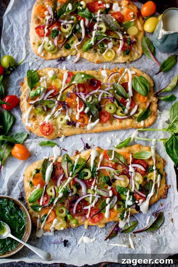 Summer Tomato Pizza with Basil Garlic Butter (Vegetarian) 5 Overhead shot of a fully topped Vegetarian Summer Tomato Pizza, garnished with fresh basil, red onion, and a generous drizzle of creamy cashew sauce. The vibrant ingredients create an inviting and wholesome meal.
