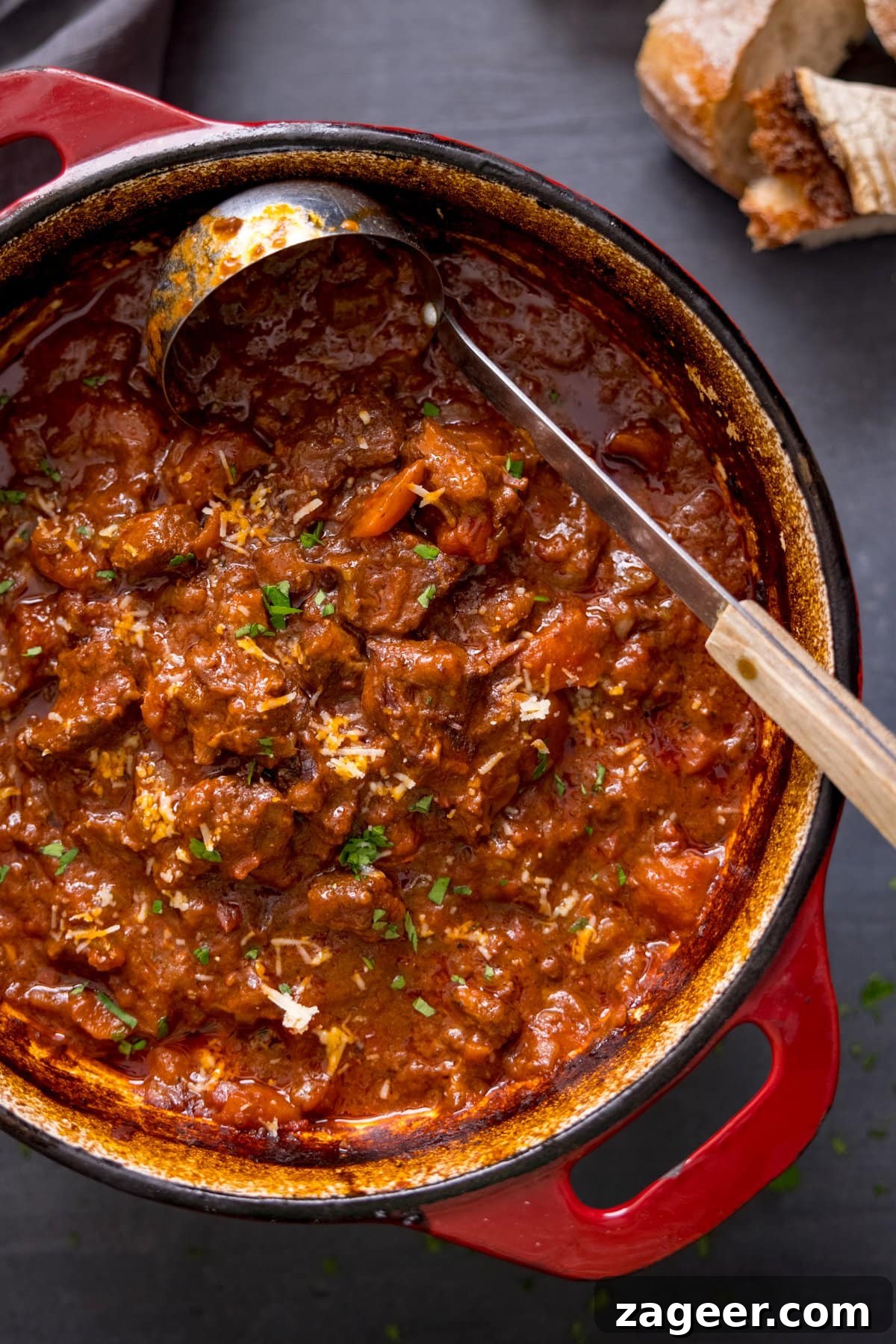 Hearty Beef Ragu Ready to Serve Overhead image of beef ragu in a red cast iron pan with a ladle, showing its rich texture.