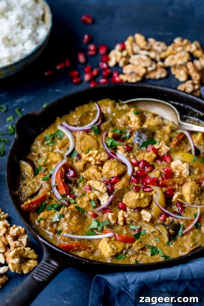 Persian Style Chicken Curry With Walnuts and Pomegranate in a cast iron skillet, garnished with fresh herbs and pomegranate seeds.