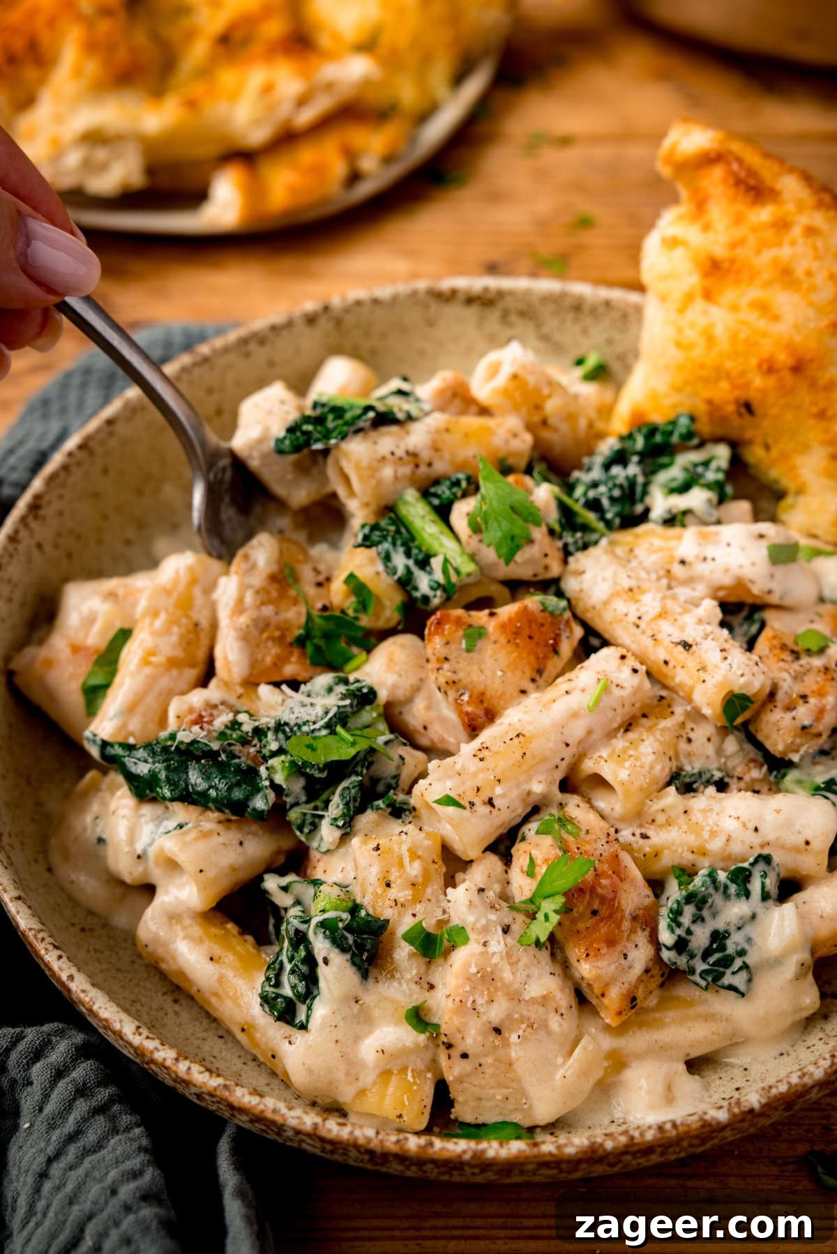 One-Pot Creamy Chicken Rigatoni Alfredo 6 Bowl of creamy chicken rigatoni alfredo pasta with kale, garnished with parsley and served with a slice of garlic bread.