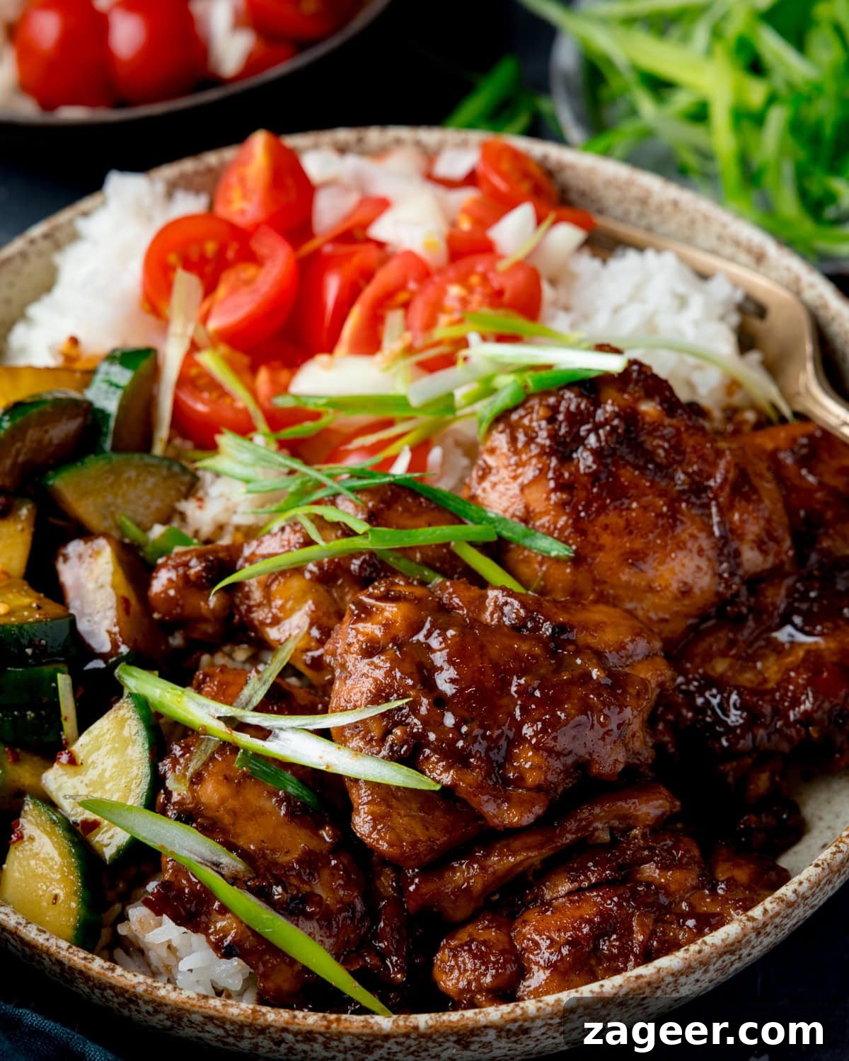 Authentic Filipino Chicken Adobo 5 A bowl with white rice, Chicken Adobo, Asian cucumber salad, sliced cherry tomatoes, onions, and spring onions, demonstrating a complete meal. Two further dishes with sliced spring onions and a tomato and onion salad are at the top of the image.