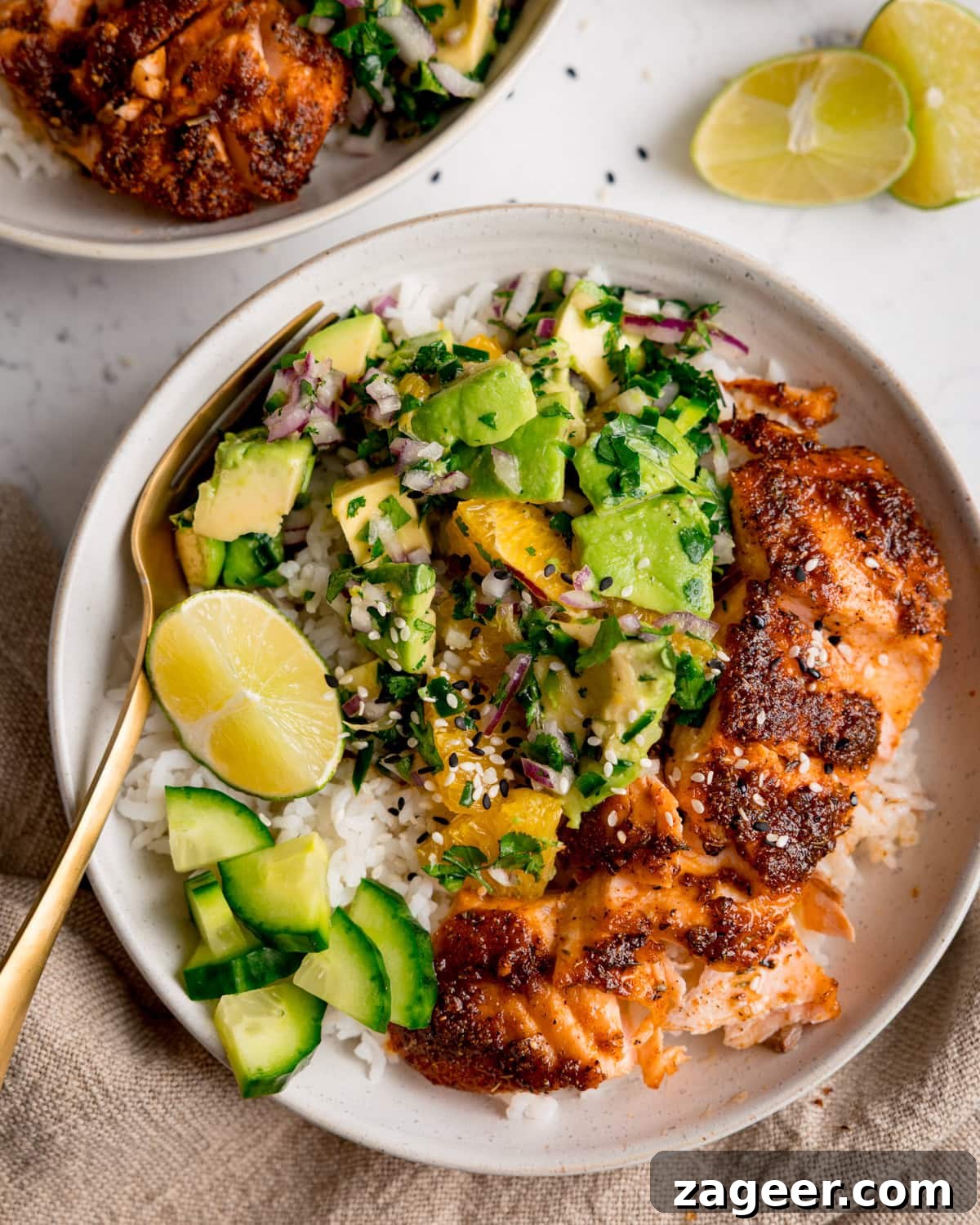 Crispy Air-Fried Salmon Bowl with Zesty Avocado-Orange Salsa 2 A salmon bowl with spiced air fryer salmon, fluffy white rice, vibrant avocado orange salsa, crisp cucumber slices, and refreshing lime wedges, with a fork ready on the side.