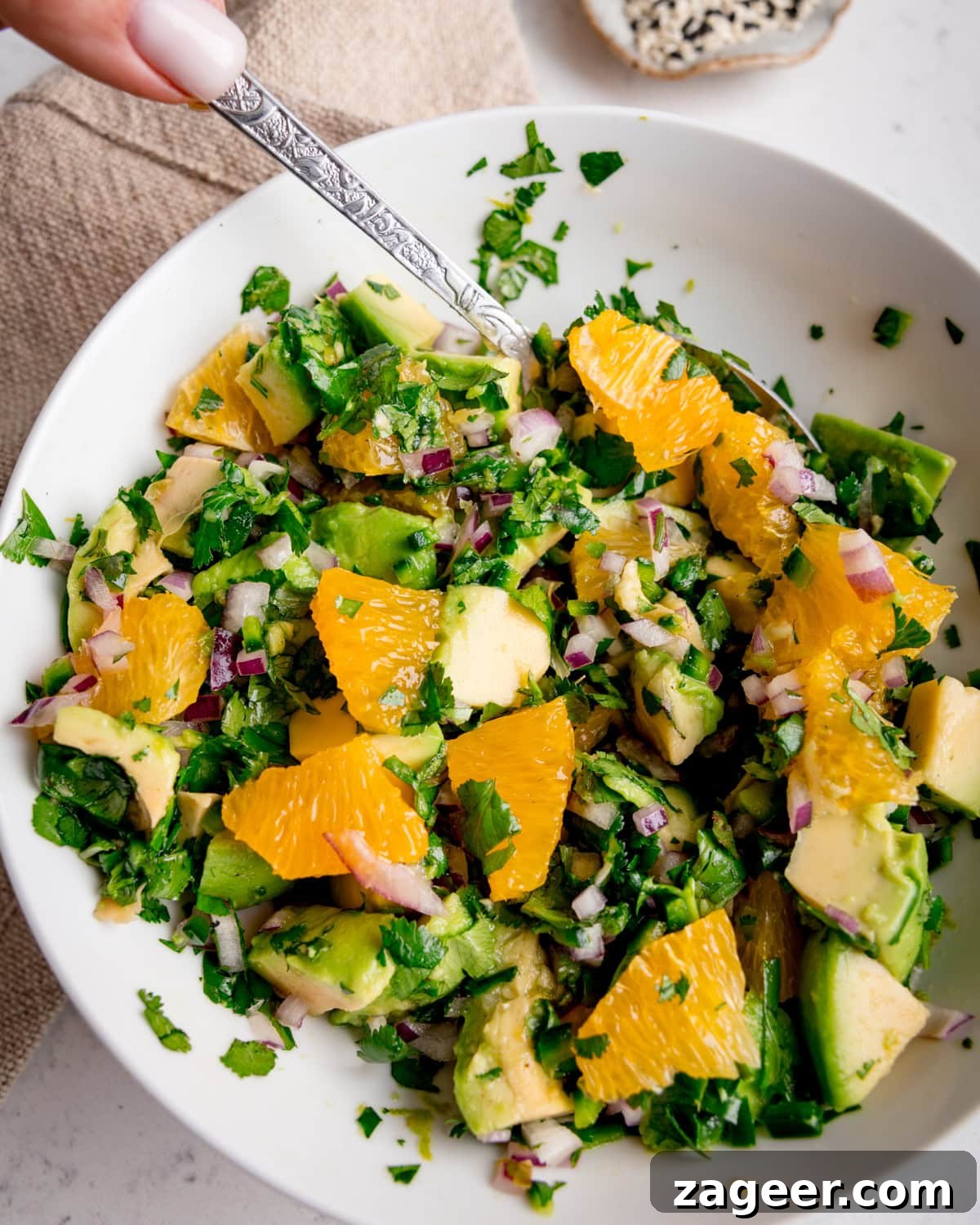 Crispy Air-Fried Salmon Bowl with Zesty Avocado-Orange Salsa 6 A white ceramic bowl filled with freshly prepared avocado orange salsa, featuring diced avocado, bright orange segments, red onion, and coriander, with a spoon dipping into the salsa.
