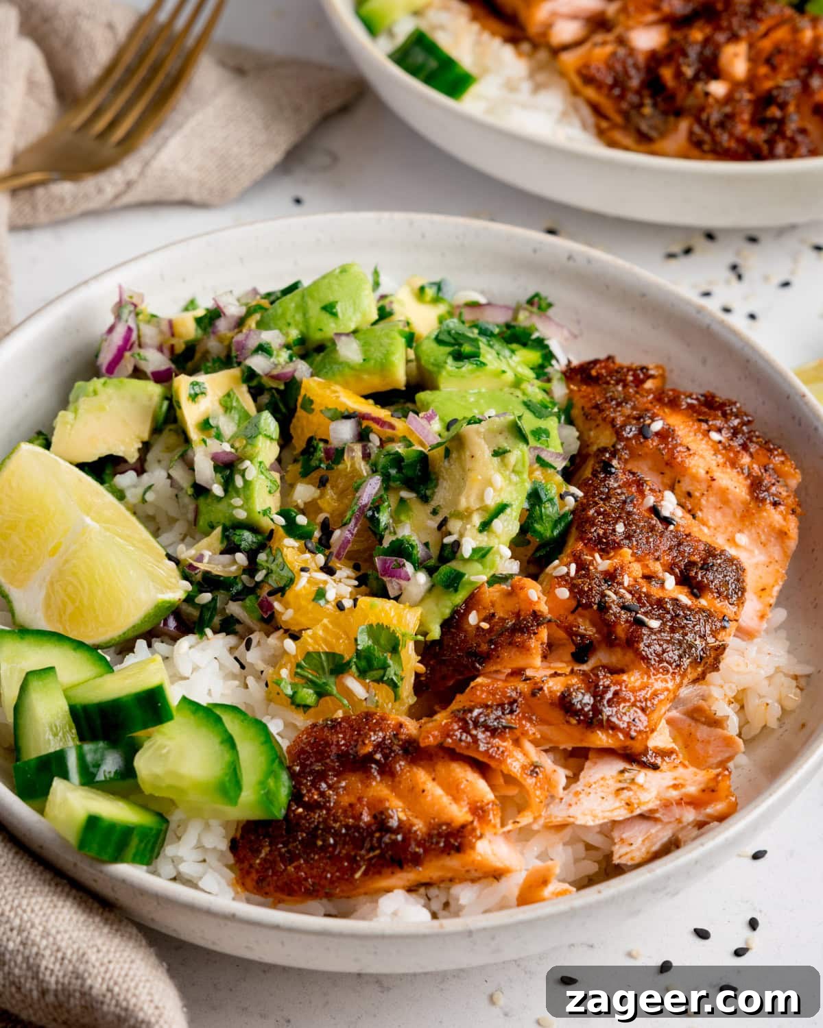 Crispy Air-Fried Salmon Bowl with Zesty Avocado-Orange Salsa 7 A beautifully presented salmon bowl with spiced air fryer salmon atop a bed of white rice, generously garnished with vibrant avocado orange salsa, fresh cucumber pieces, a sprinkle of fresh coriander, and bright lime wedges.