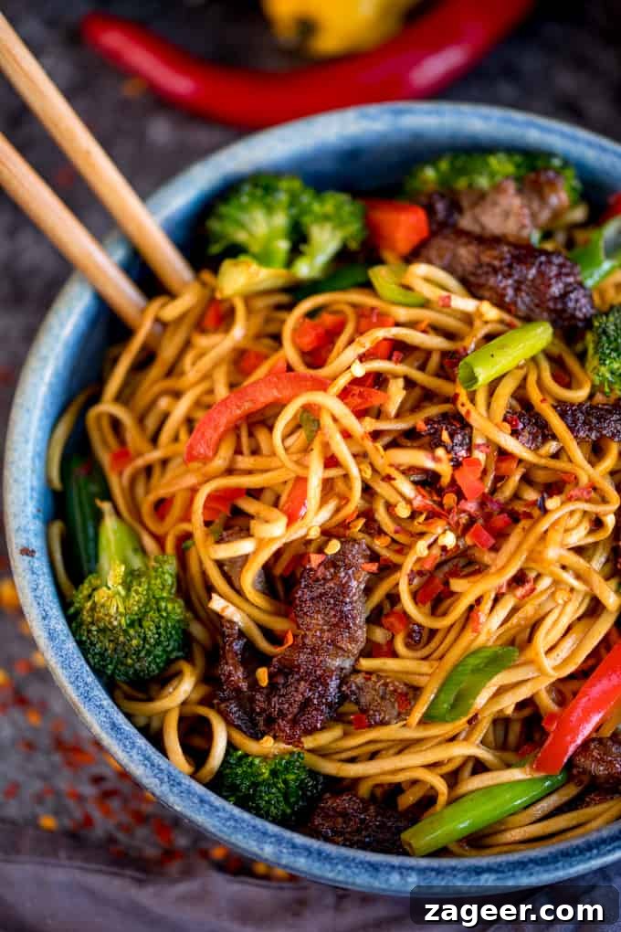Crispy Chili Beef Noodles Recipe for Flavorful Weeknight Dinner 2 Overhead image of crispy chilli beef noodles with red pepper and broccoli in a blue bowl. There is a pair of chopsticks sticking out of the bowl.