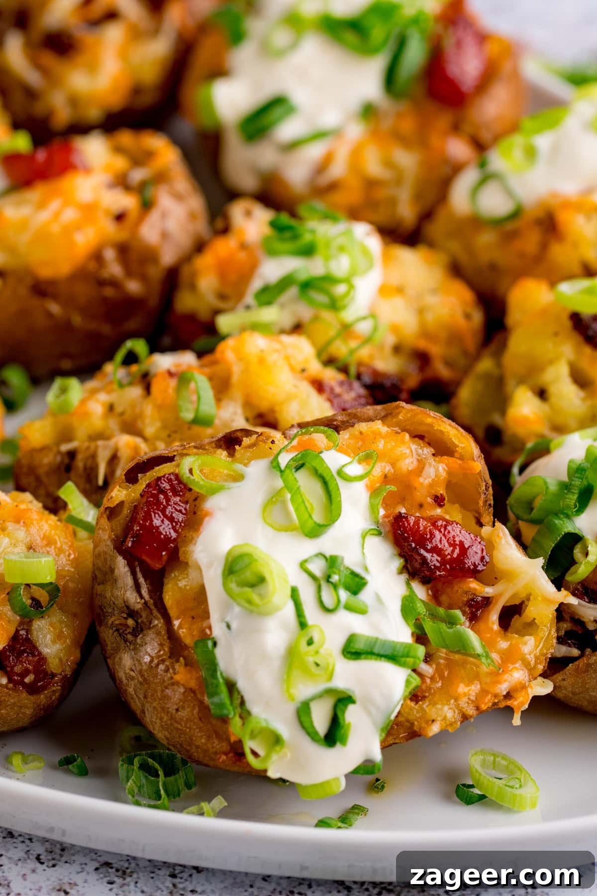 Crispy Loaded Potato Skins with Cheddar, Bacon & Sour Cream 6 Baked cheese and bacon potato skins topped with soured cream and chopped spring onions, served on a white plate.