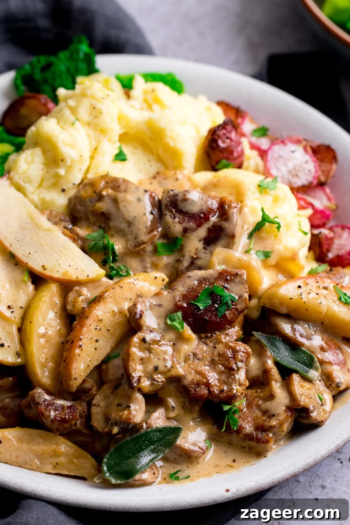 Creamy Pork and Apple Casserole Recipe with Herbed Crust 7 Close up of creamy pork and apple casserole on a white plate with mashed potatoes and roasted radishes.
