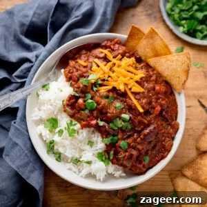 Authentic Chilli Con Carne Recipe with Smoky Beef and Beans 19 A bowl of chilli con carne with kidney beans, ground beef, cheese, and cilantro over white rice. Tortilla chips on the side.