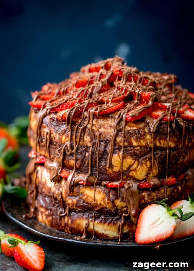 Tall image of a four layer chocolate bread and butter pudding round cake on a black plate. Nutella and strawberries on the top and in the middle. Cake is slightly cropped on the right hand side. Dark blue background, strawberries scattered around.