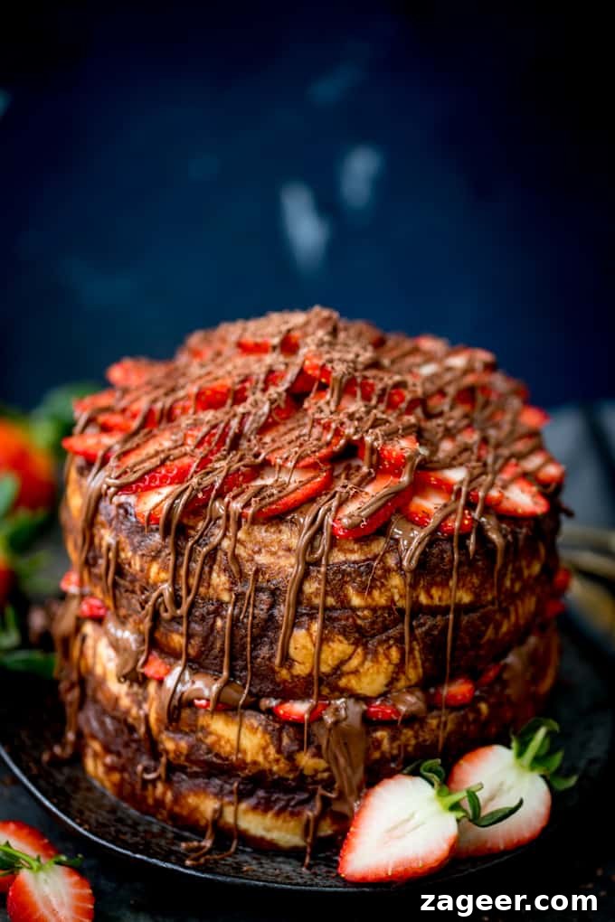 Tall image of a centre-aligned four layer chocolate bread and butter pudding round cake on a black plate. Nutella and strawberries on the top and in the middle. Dark blue background, strawberries scattered around.